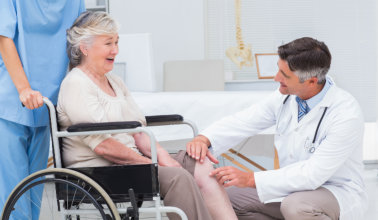 Male orthopedic doctor examining senior womans knee in clinic